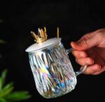 ⁦مج زجاج متعرج 450 ملي بغطاء تاج ومعلقة استانليس ستيل جولد للمشروبات الباردة والساخنة بيد⁩ - الصورة ⁦3⁩